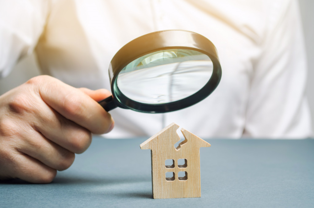 man with a magnifying glass looks at a house with a crack