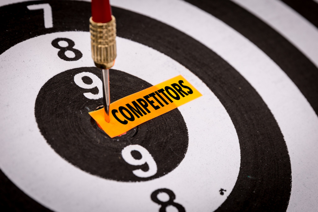 the word "competitors" written on a yellow paper pinned to a dartboard