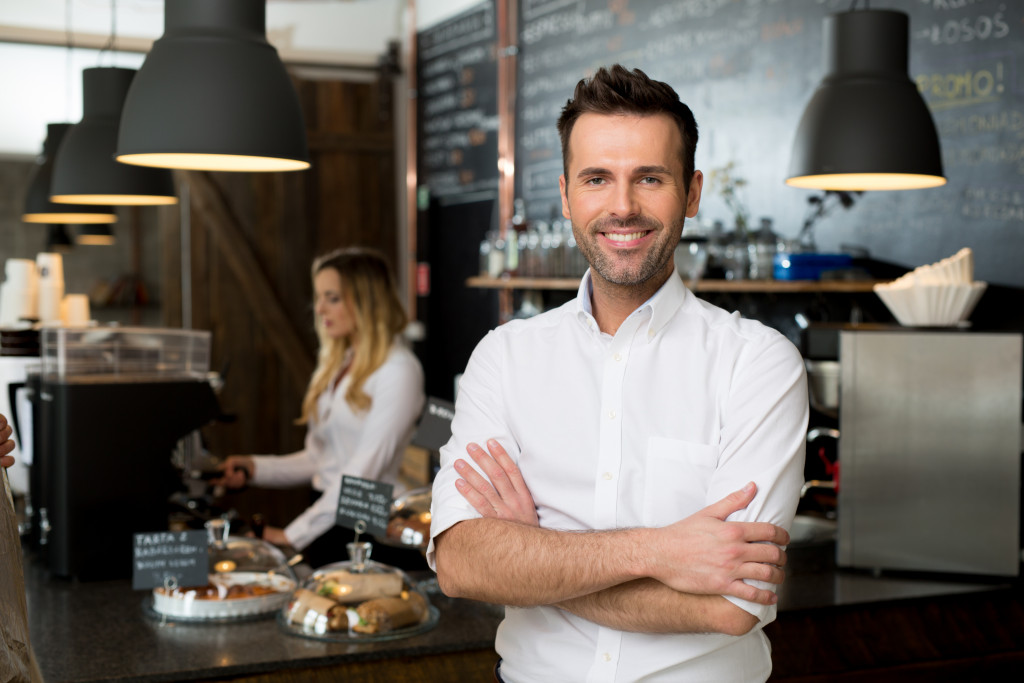 Small business owner standing inside a coffee shop with an employee preparing coffee in the background.