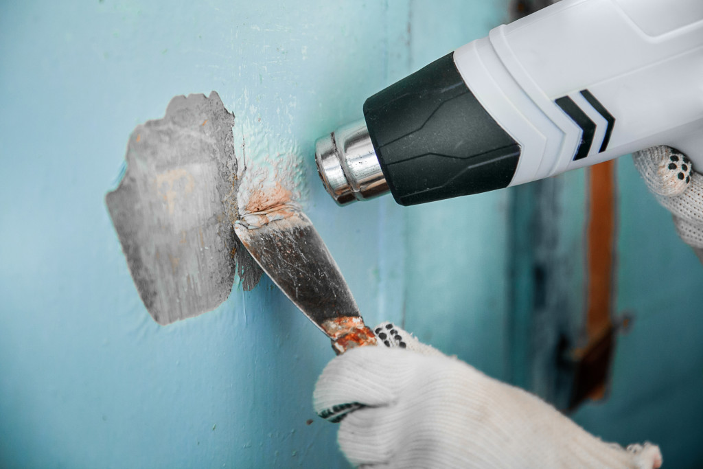 Removing old paint from concrete wall with heat gun and scraper